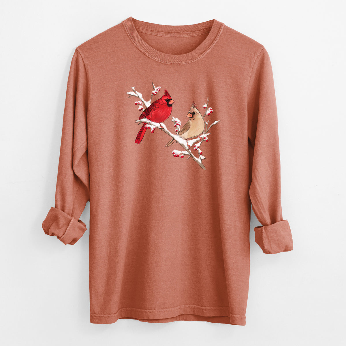 Yam burnt orange Comfort Colors long sleeve shirt laid flat with the cuffs rolled, printed with a full-color illustration of a male and female northern cardinal perched on a snowy branch with red berries.