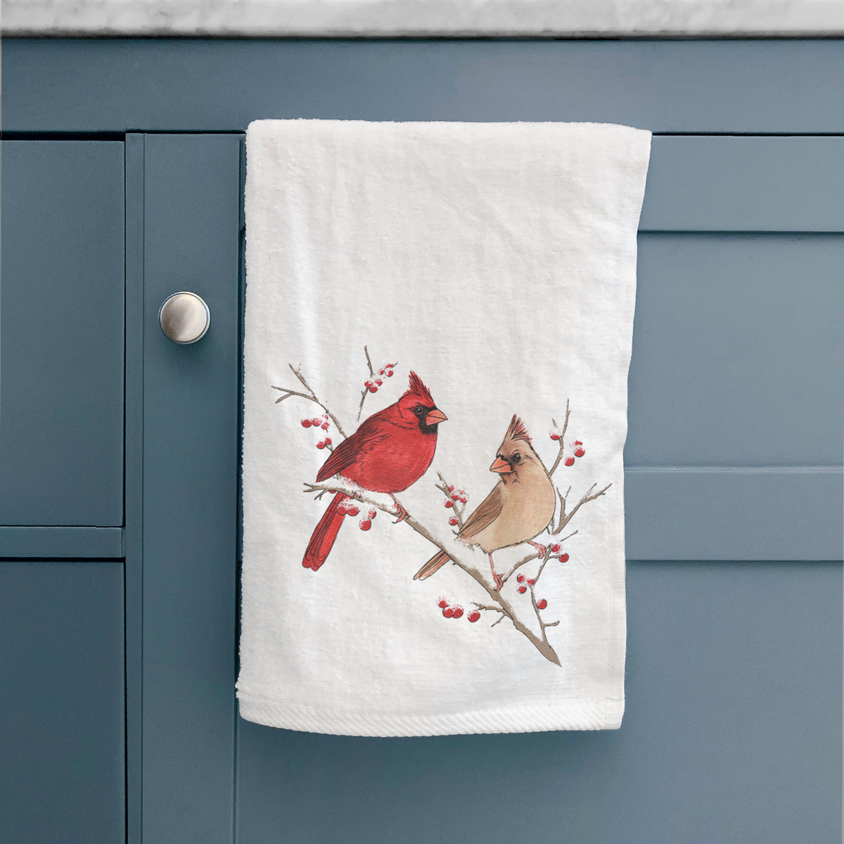 White hand towel printed with a full-color illustration of a male and female northern cardinal perched on a snowy branch with red berries, hanging on a cabinet door.