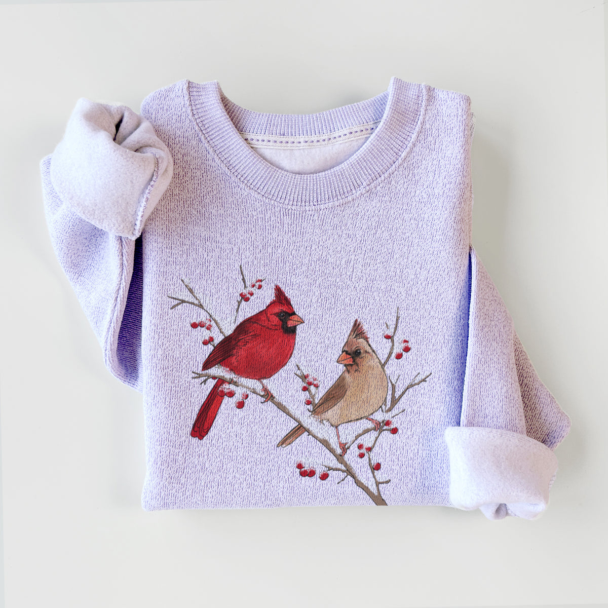 Ice purple knit sweatshirt printed with a full-color illustration of a male and female northern cardinal perched on a snowy branch with red berries, styled flat.