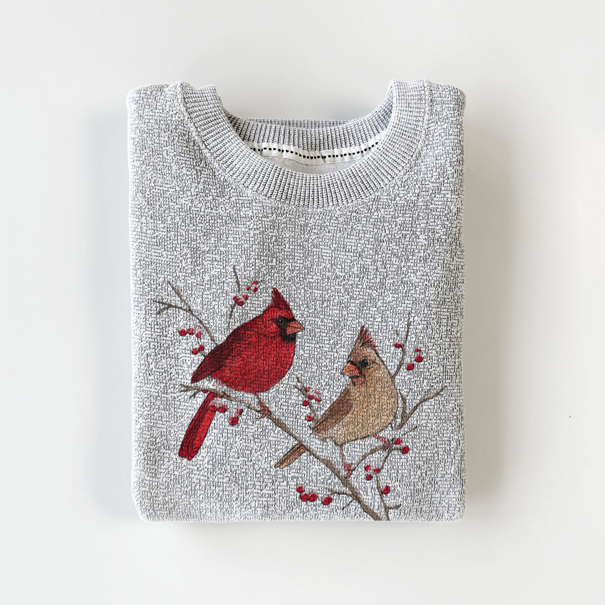 Salt and pepper knit sweatshirt printed with a full-color illustration of a male and female northern cardinal perched on a snowy branch with red berries, styled flat.