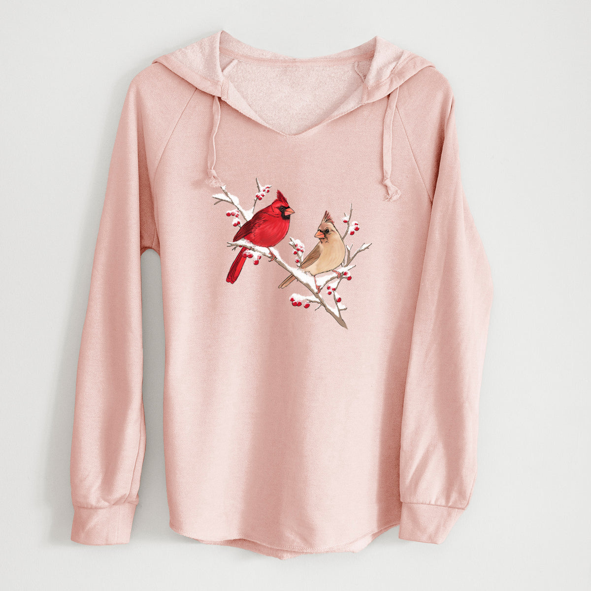 Blush pink women's Cali Wave hooded sweatshirt laid flat, printed with a full-color illustration of a male and female northern cardinal perched on a snowy branch with red berries.