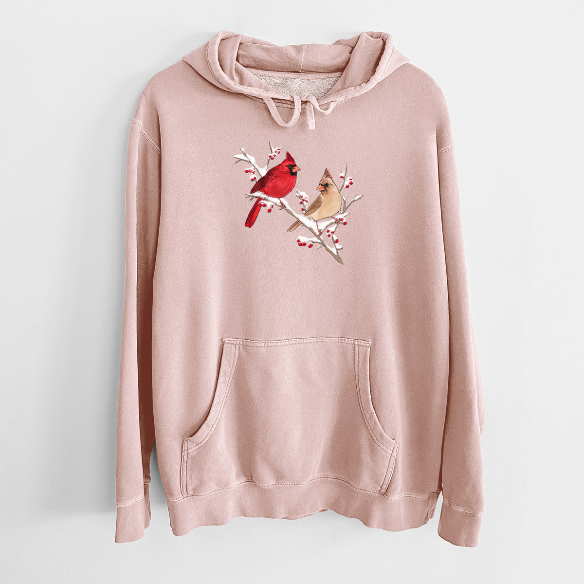 Dusty pink pigment dyed hoodie laid flat, printed with a full-color illustration of a male and female northern cardinal perched on a snowy branch with red berries.