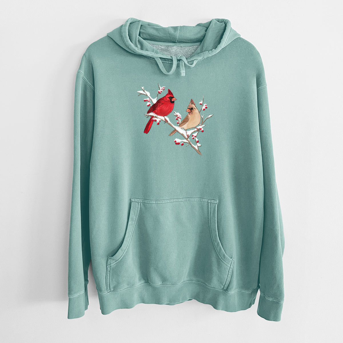 Mint green pigment dyed hoodie laid flat, printed with a full-color illustration of a male and female northern cardinal perched on a snowy branch with red berries.