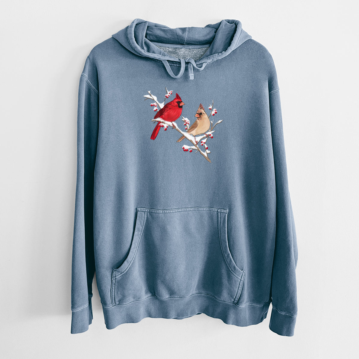 Slate blue pigment dyed hoodie laid flat, printed with a full-color illustration of a male and female northern cardinal perched on a snowy branch with red berries.