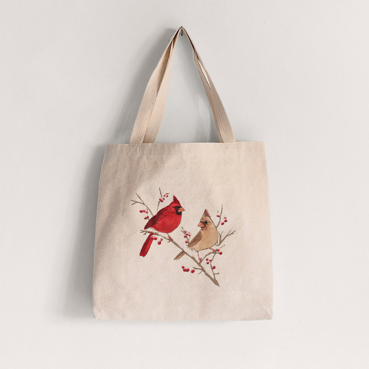 Natural canvas tote bag printed with a full-color illustration of a male and female northern cardinal perched on a snowy branch with red berries.