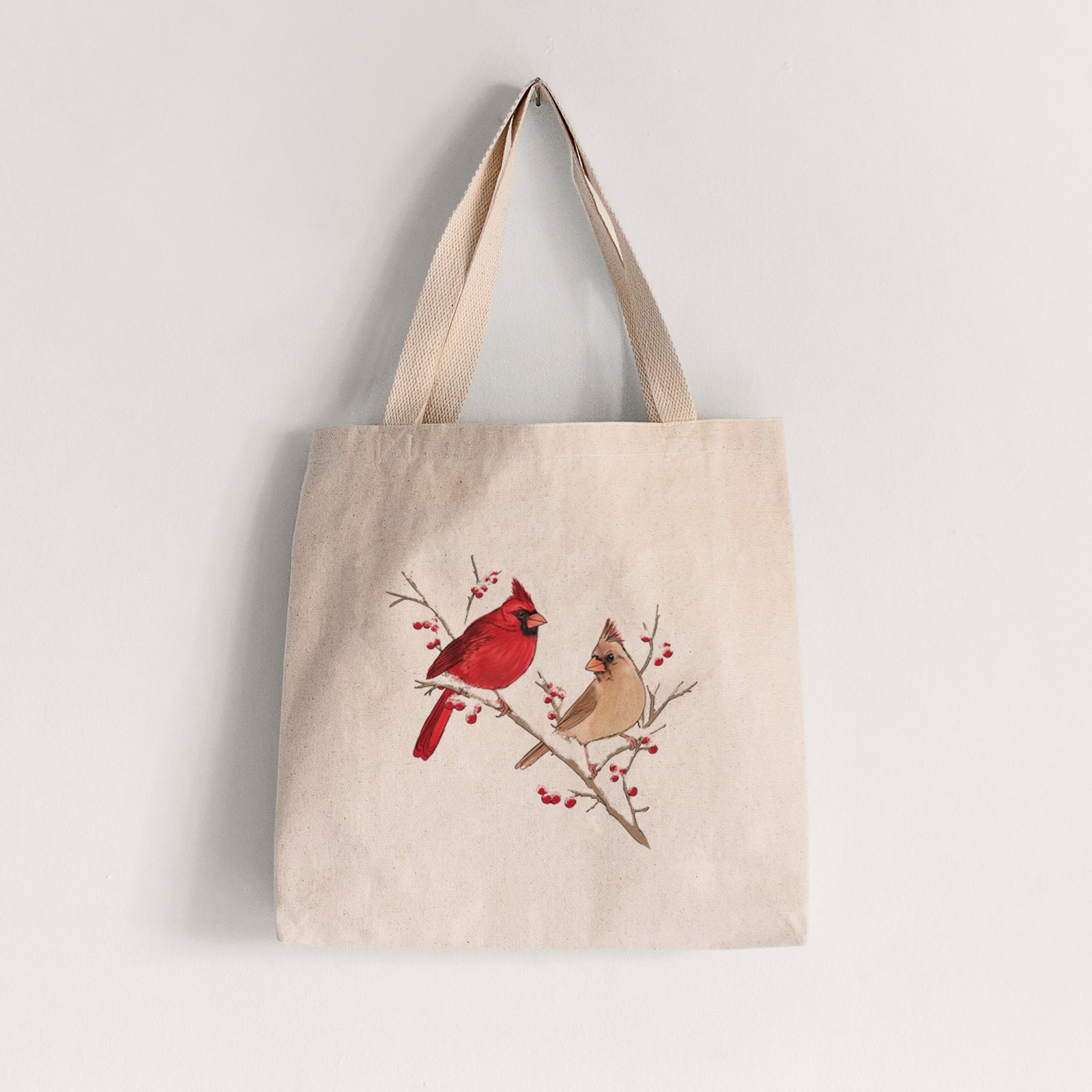 Natural canvas tote bag printed with a full-color illustration of a male and female northern cardinal perched on a snowy branch with red berries.