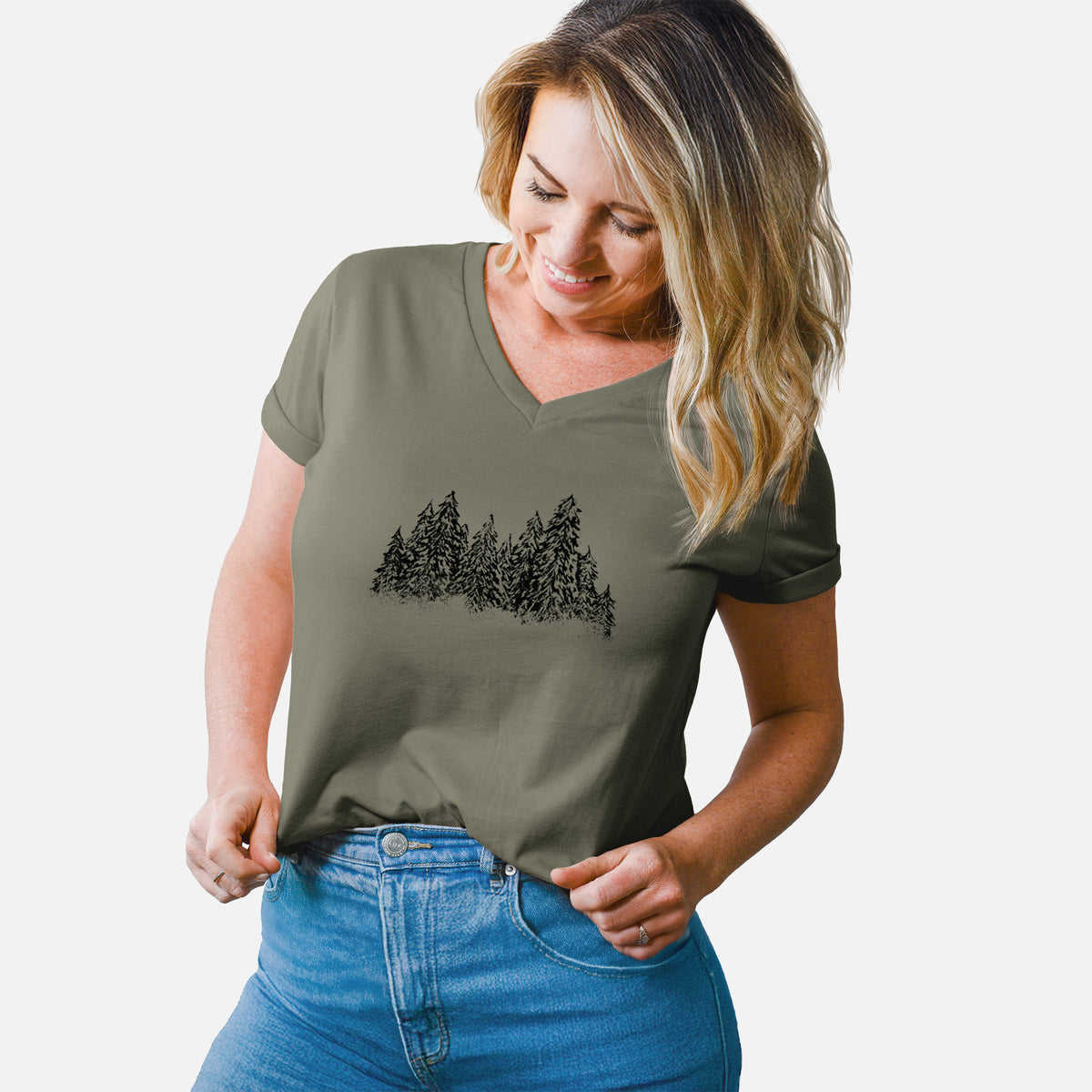 Woman wearing a military green women's relaxed fit cotton V-neck t-shirt printed with a black ink illustration of a row of snow-dusted evergreen trees.