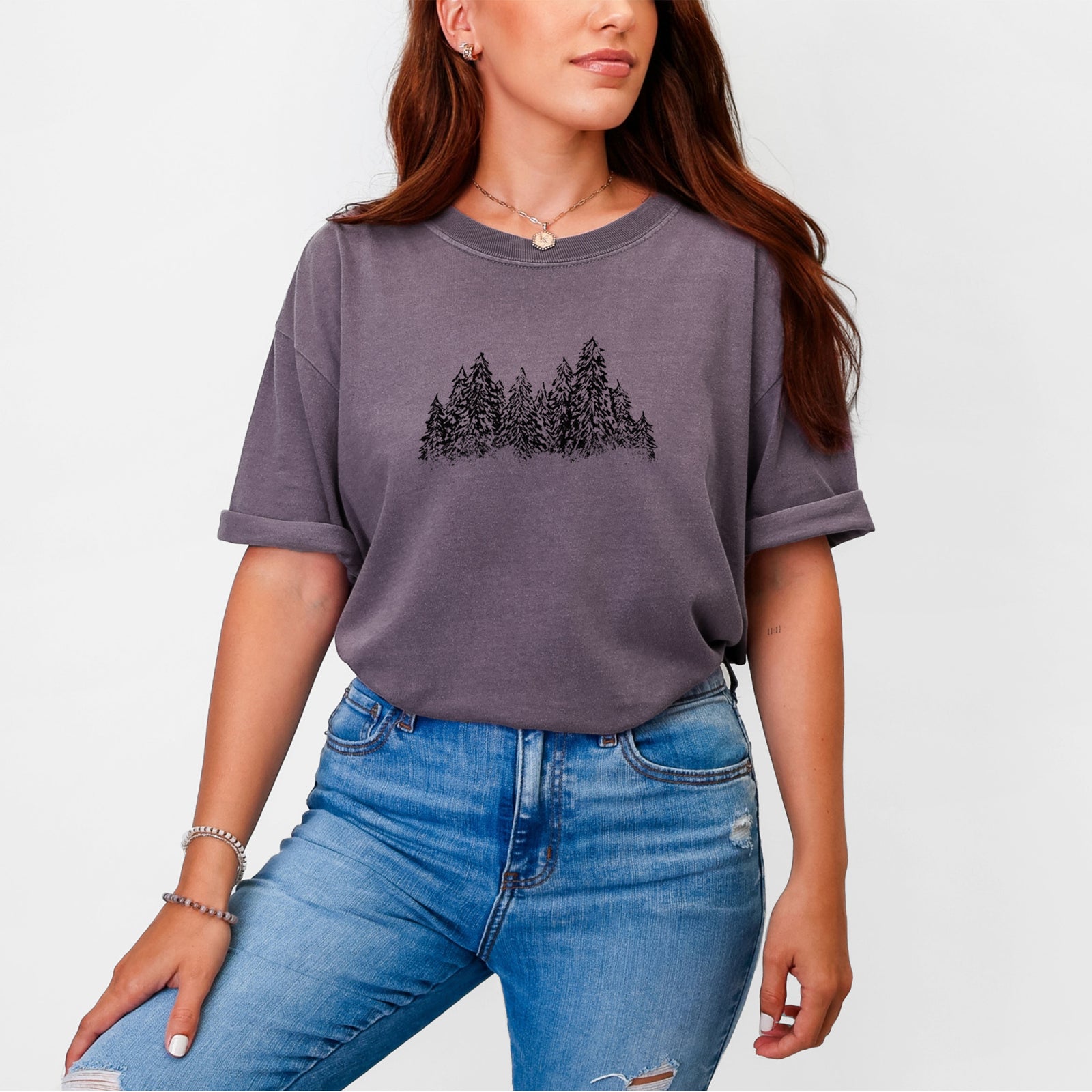 Blue jean Comfort Colors t-shirt laid flat, printed with a black ink illustration of a row of snow-dusted evergreen trees.
