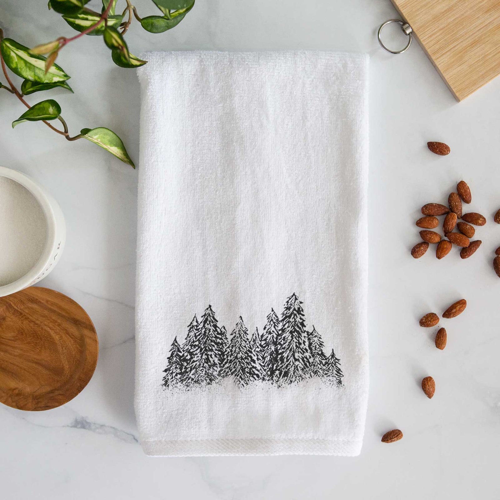 White hand towel printed with a black ink illustration of a row of snow-dusted evergreen trees.