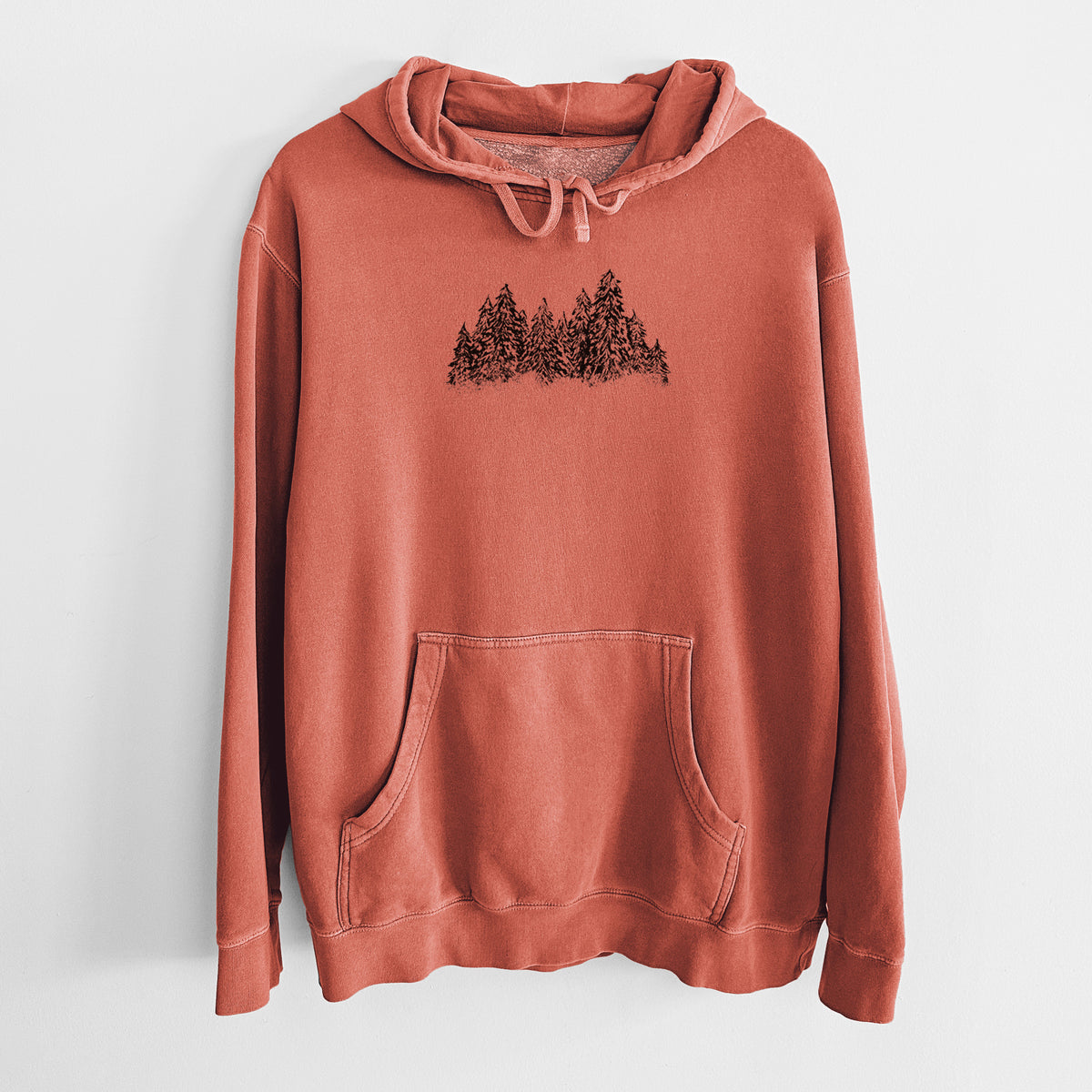 Amber orange pigment dyed hoodie laid flat, printed with a black ink illustration of a row of snow-dusted evergreen trees.