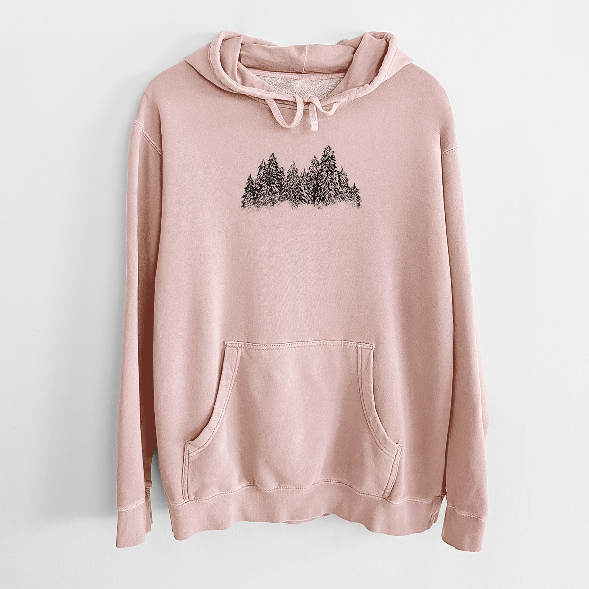 Dusty pink pigment dyed hoodie laid flat, printed with a black ink illustration of a row of snow-dusted evergreen trees.