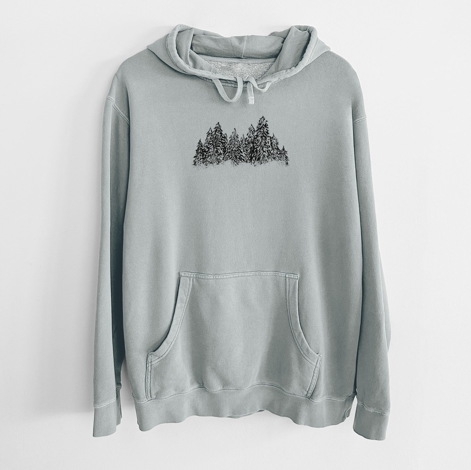 Sage green pigment dyed hoodie laid flat, printed with a black ink illustration of a row of snow-dusted evergreen trees.