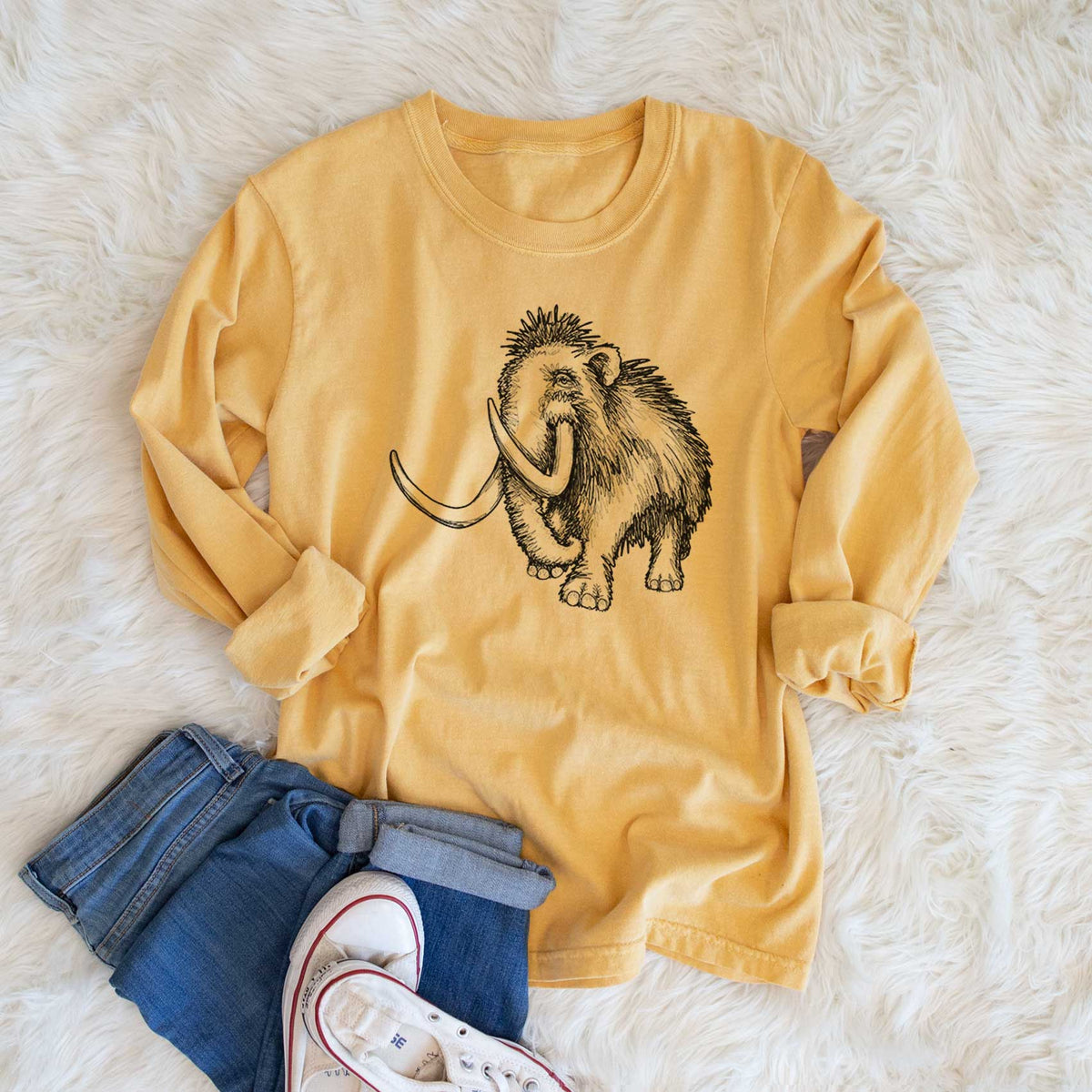 Golden wheat yellow Comfort Colors long sleeve shirt printed with a black ink illustration of a woolly mammoth with long curved tusks, shown in a lifestyle photo.