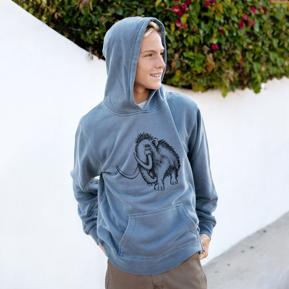Boy wearing a youth pigment dyed hoodie printed with a black ink illustration of a woolly mammoth with long curved tusks.