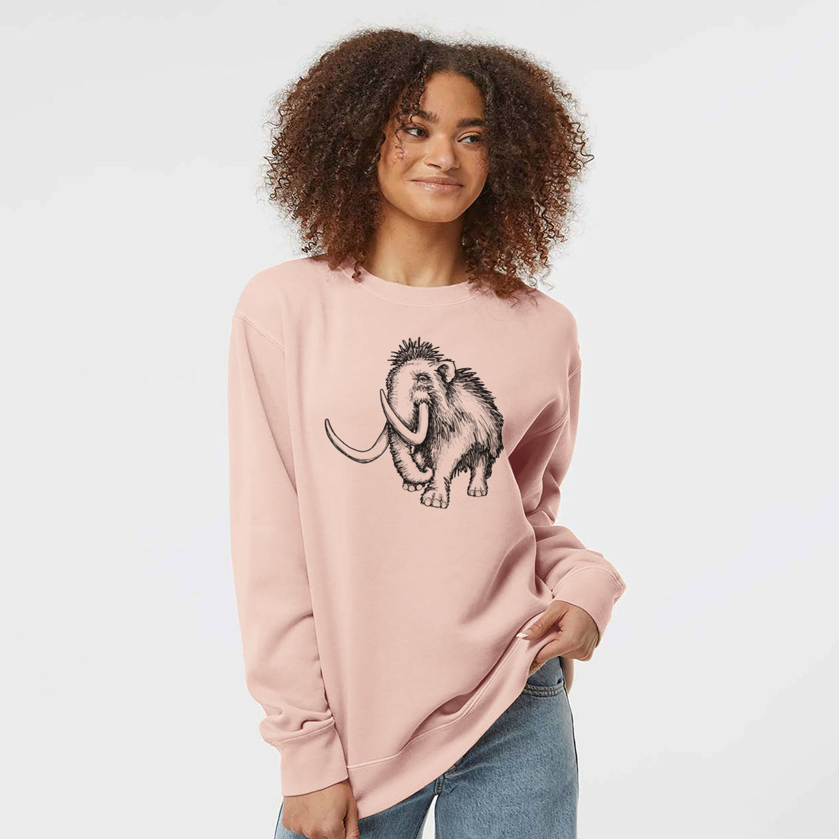 Model wearing a dusty pink pigment dyed crewneck sweatshirt printed with a black ink illustration of a woolly mammoth with long curved tusks.