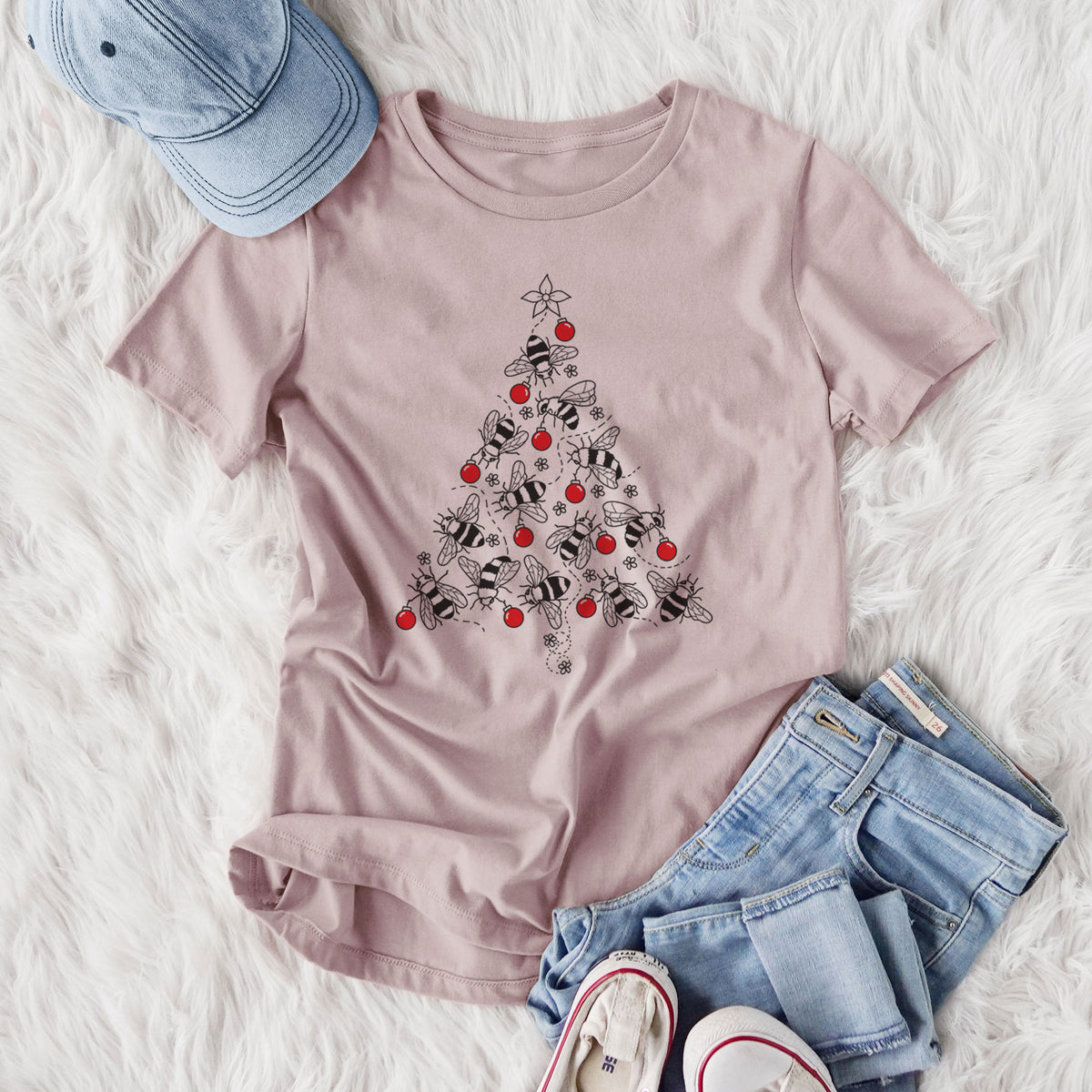 Women's relaxed fit cotton t-shirt printed with a Christmas tree made of black ink bees with red ornaments and a star on top, styled flat on a white faux fur rug with jeans.