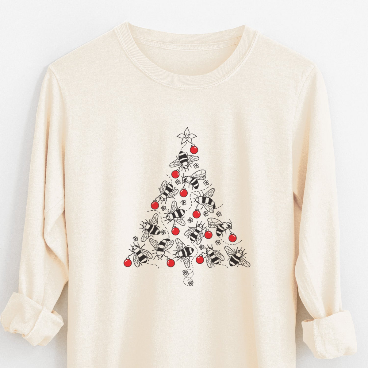 Ivory Comfort Colors long sleeve shirt laid flat with the cuffs rolled, printed with a Christmas tree made of black ink bees with red ornaments and a star on top.