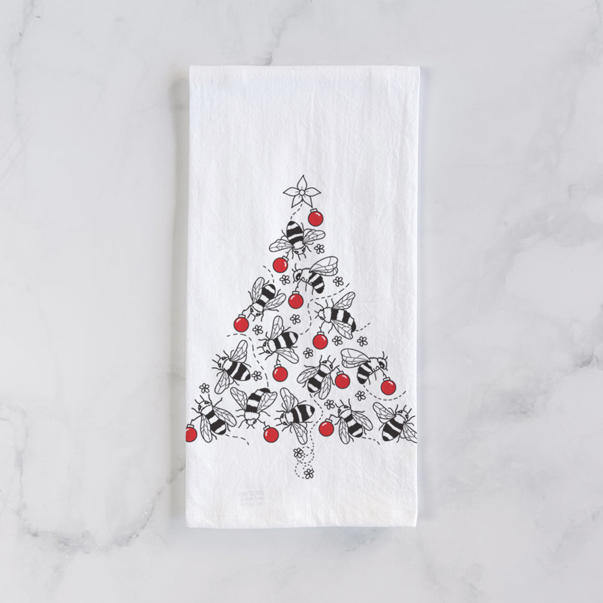 White cotton tea towel laid flat on marble, printed with a Christmas tree made of black ink bees with red ornaments and a star on top.