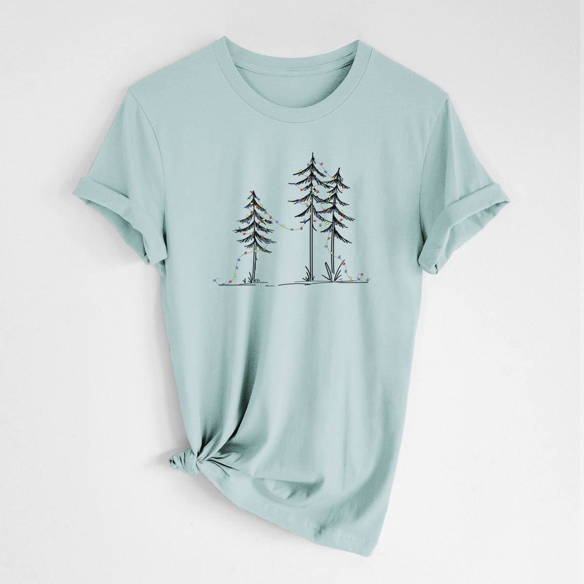 Dusty blue lightweight cotton t-shirt laid flat with the sleeves rolled, printed with three slender black ink pine trees strung with a garland of multicolored holiday lights.