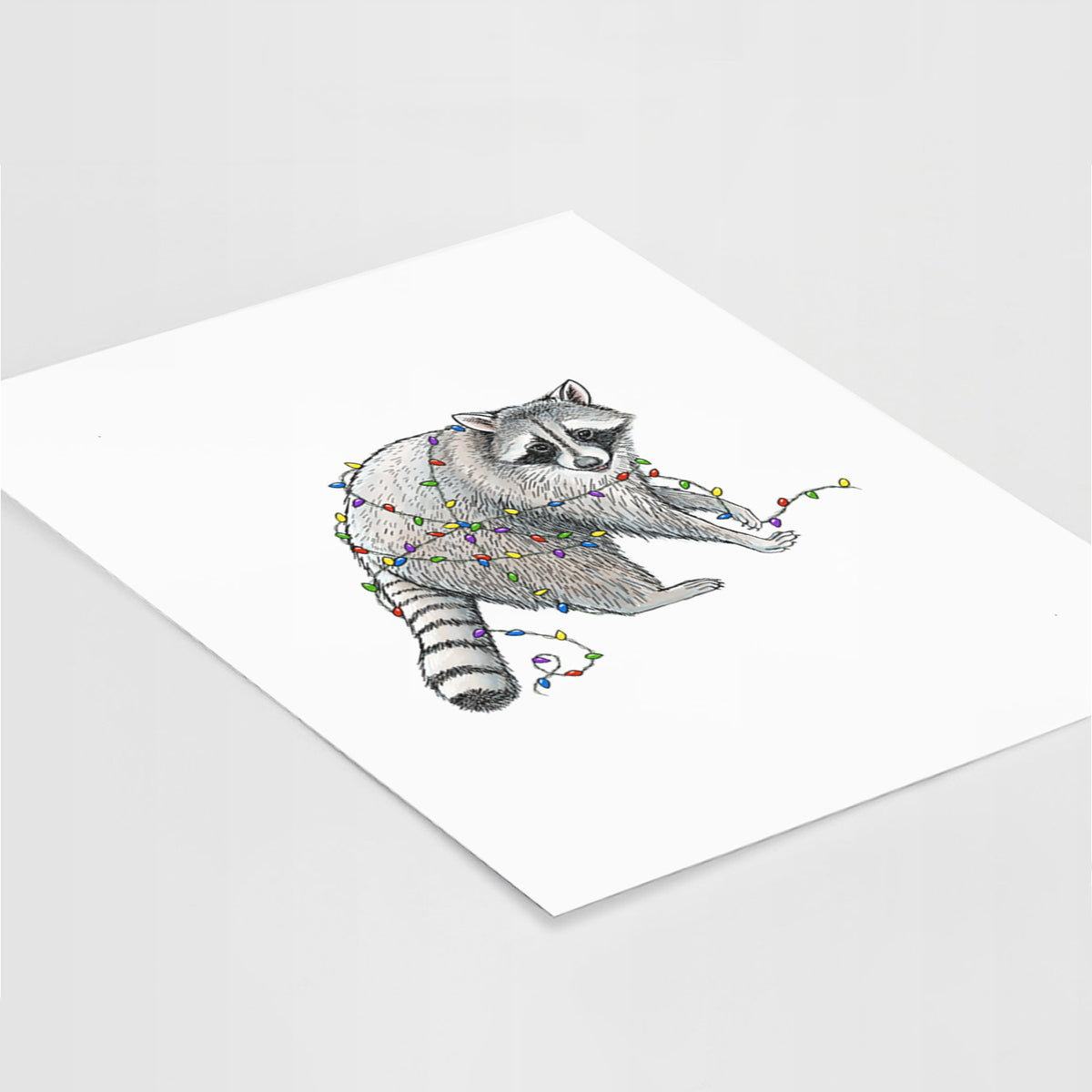 Art print of a black ink raccoon tangled in a string of colorful holiday lights, lying at an angle on a white surface.
