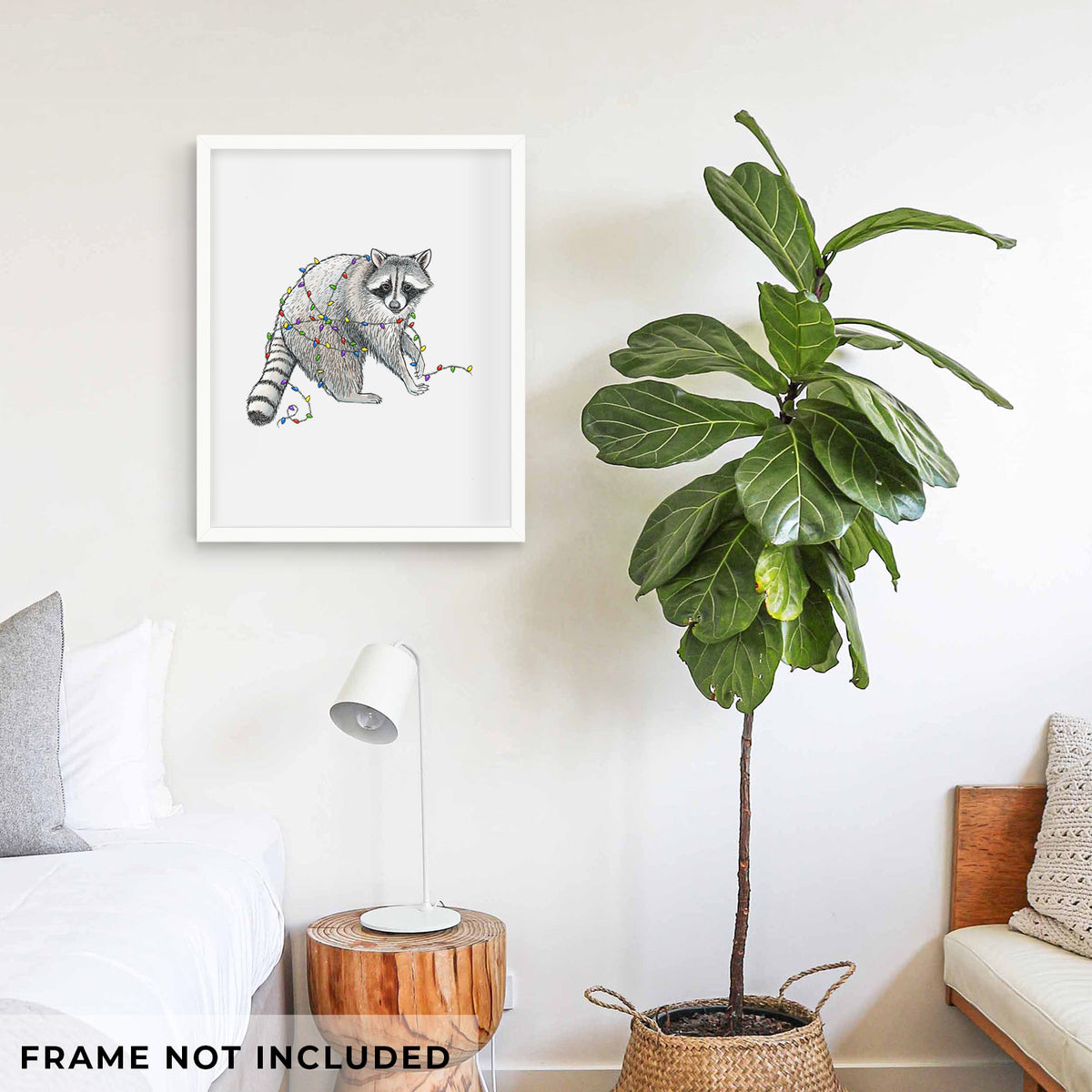 Art print of a black ink raccoon tangled in a string of colorful holiday lights, shown framed on a living room wall beside a potted plant. Frame not included.