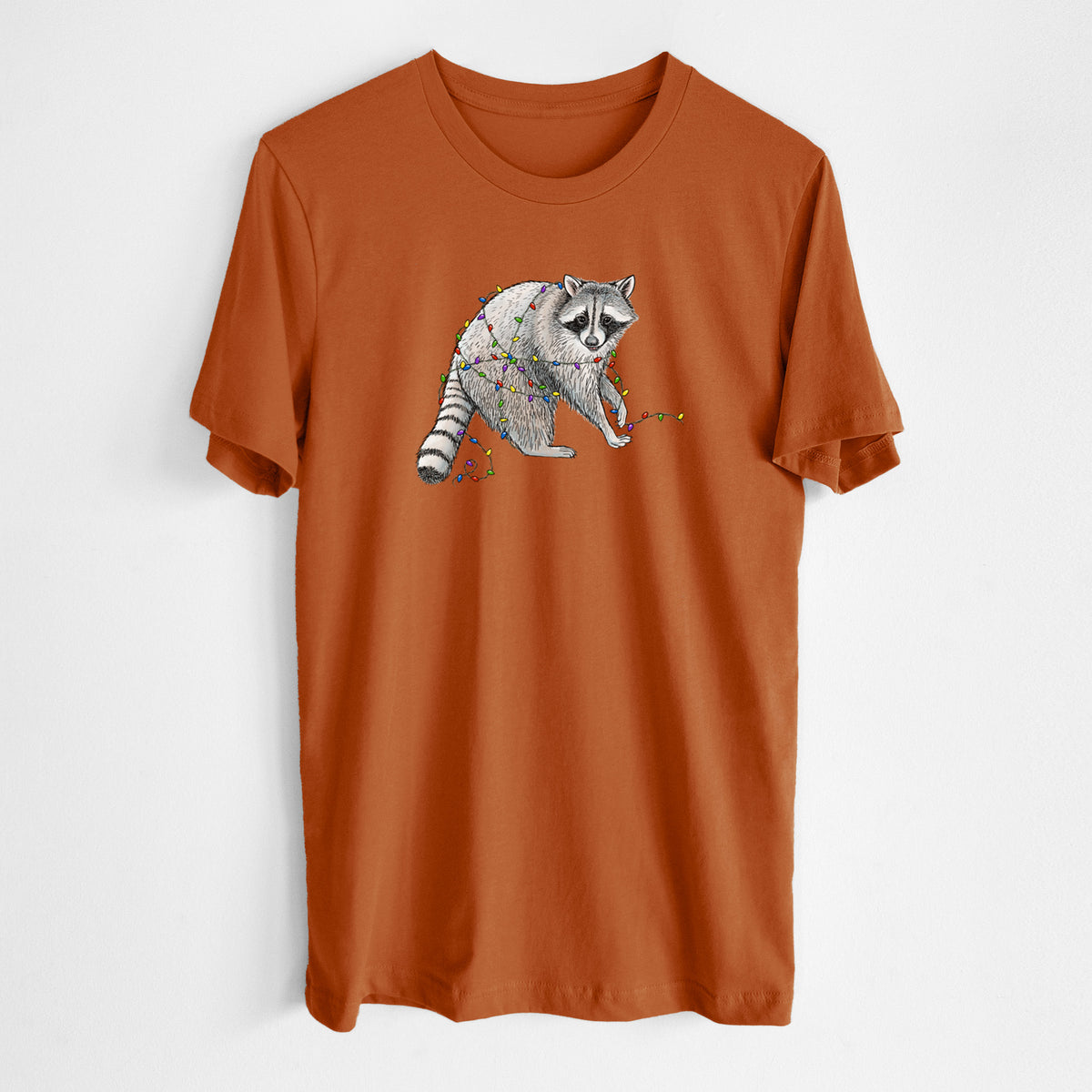Autumn lightweight cotton t-shirt laid flat, printed with a black ink raccoon tangled in a string of colorful holiday lights.