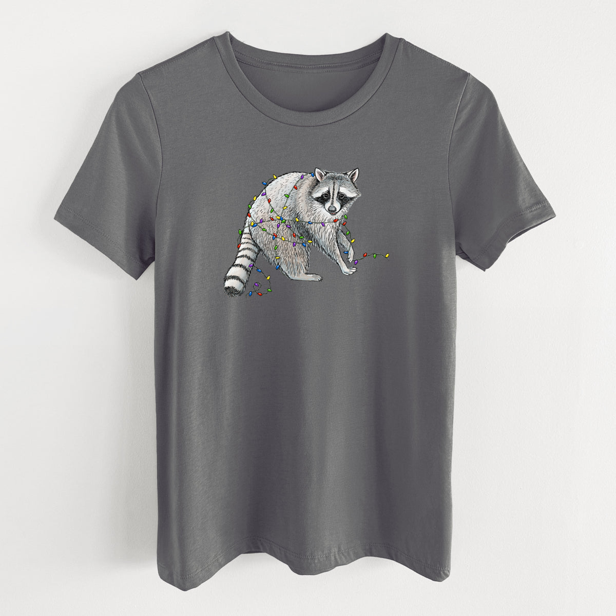 Asphalt women's relaxed fit cotton t-shirt laid flat, printed with a black ink raccoon tangled in a string of colorful holiday lights.