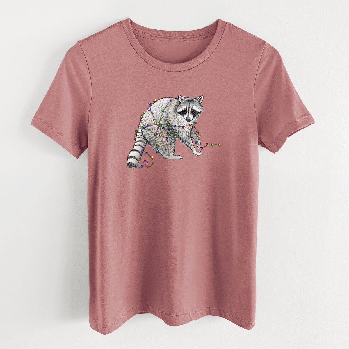 Mauve pink women's relaxed fit cotton t-shirt laid flat, printed with a black ink raccoon tangled in a string of colorful holiday lights.
