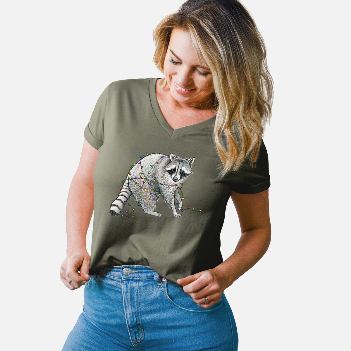 Woman wearing a military green women's relaxed fit cotton V-neck t-shirt printed with a black ink raccoon tangled in a string of colorful holiday lights.