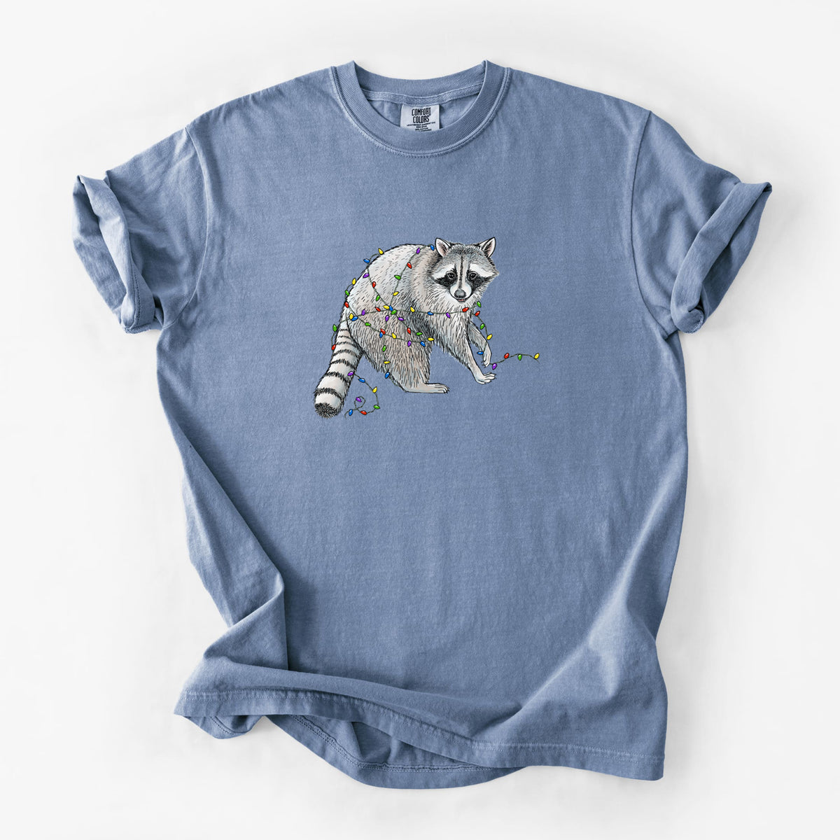 Blue jean Comfort Colors t-shirt laid flat, printed with a black ink raccoon tangled in a string of colorful holiday lights.