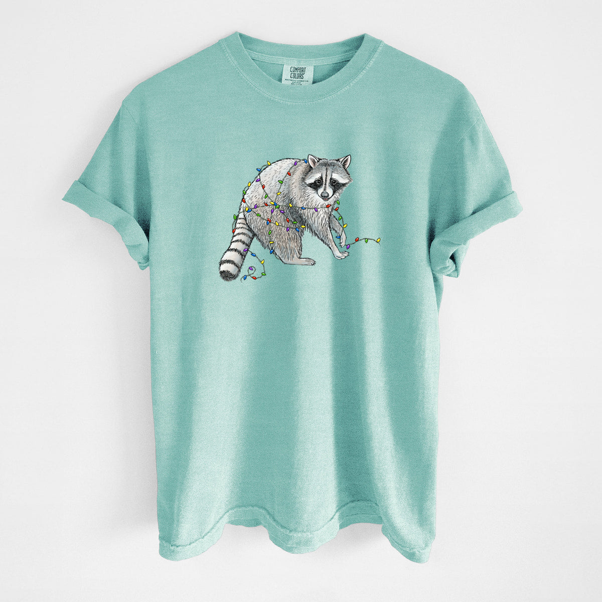 Chalky mint Comfort Colors t-shirt laid flat, printed with a black ink raccoon tangled in a string of colorful holiday lights.