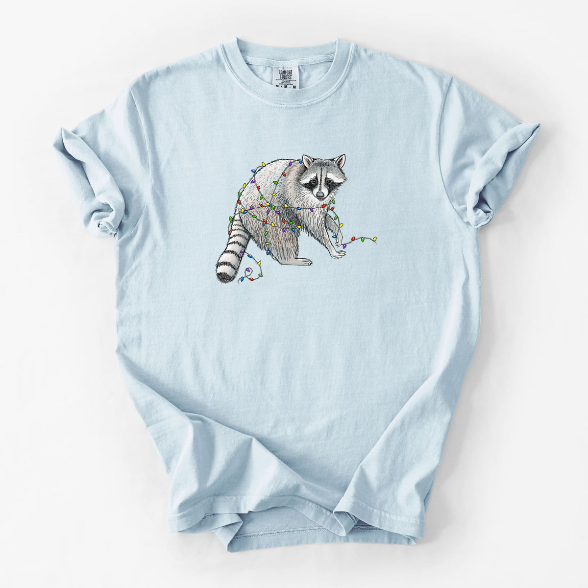 Chambray blue Comfort Colors t-shirt laid flat, printed with a black ink raccoon tangled in a string of colorful holiday lights.