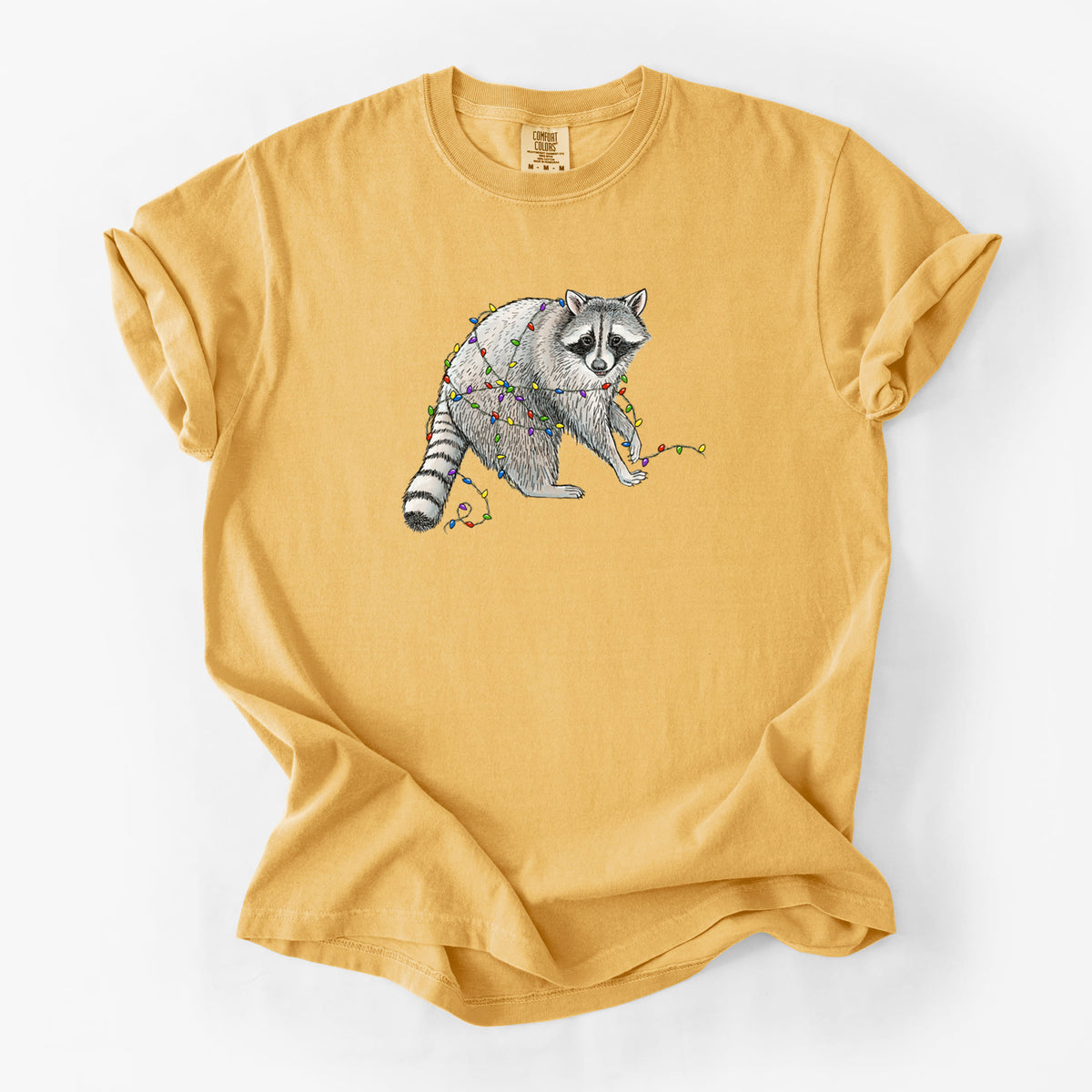 Golden wheat yellow Comfort Colors t-shirt laid flat, printed with a black ink raccoon tangled in a string of colorful holiday lights.