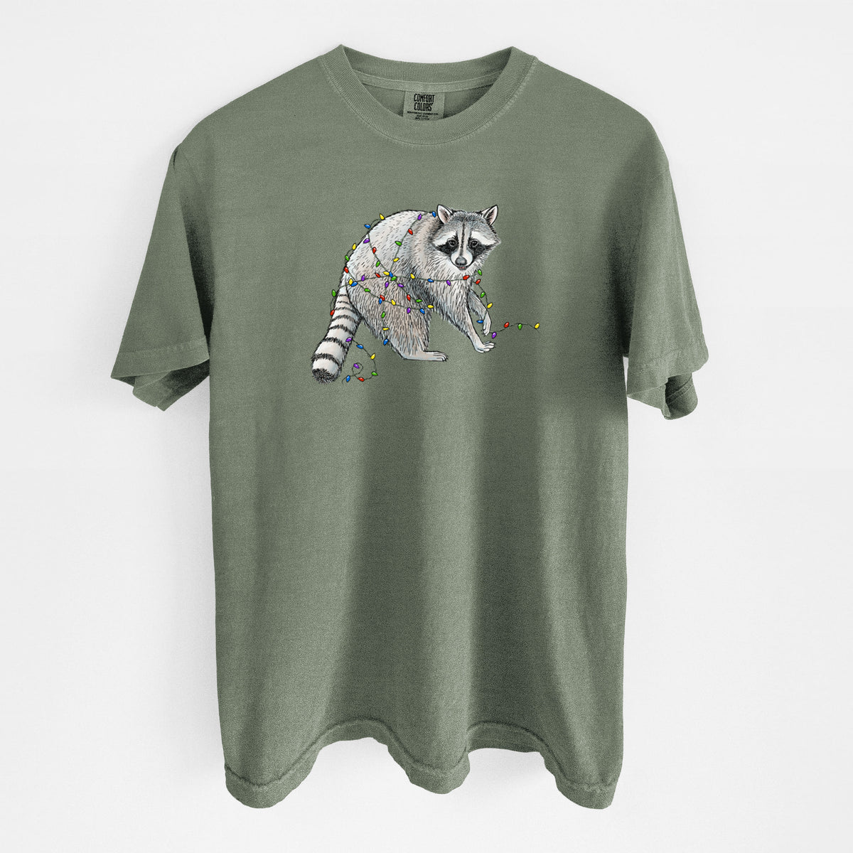 Moss green Comfort Colors t-shirt laid flat, printed with a black ink raccoon tangled in a string of colorful holiday lights.