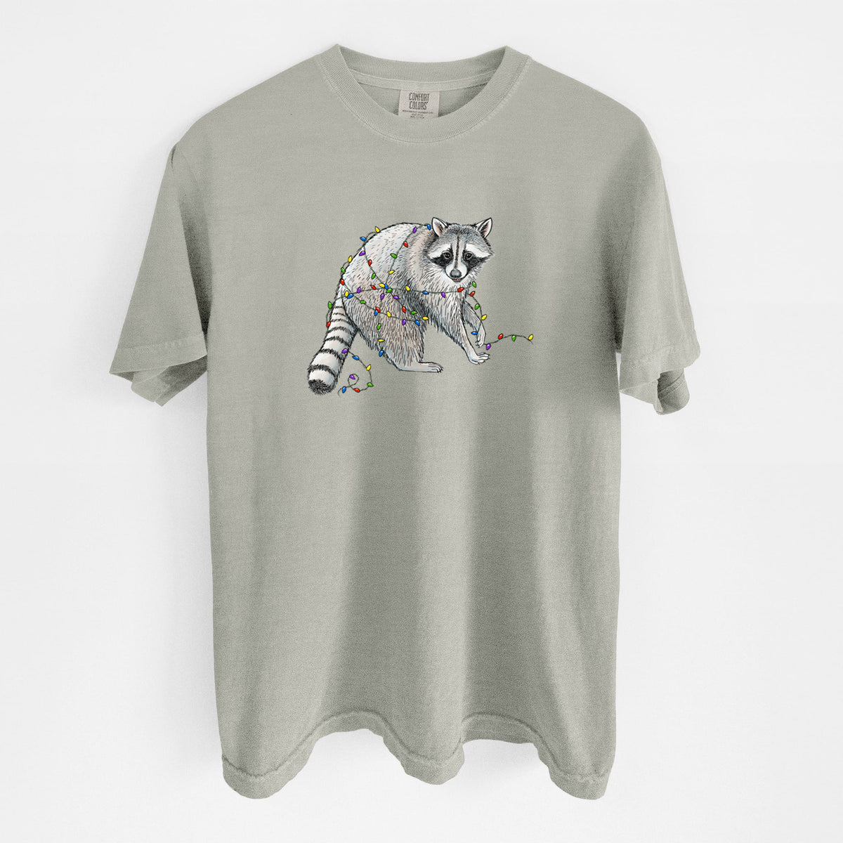 Sandstone beige Comfort Colors t-shirt laid flat, printed with a black ink raccoon tangled in a string of colorful holiday lights.