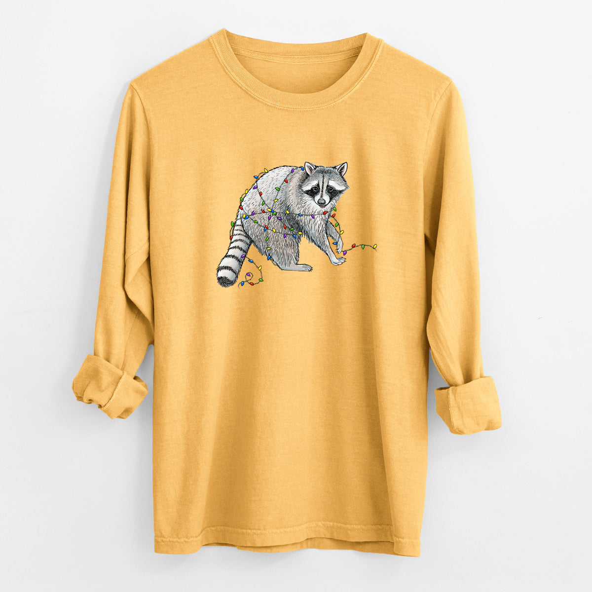Golden wheat yellow Comfort Colors long sleeve shirt laid flat with the cuffs rolled, printed with a black ink raccoon tangled in a string of colorful holiday lights.