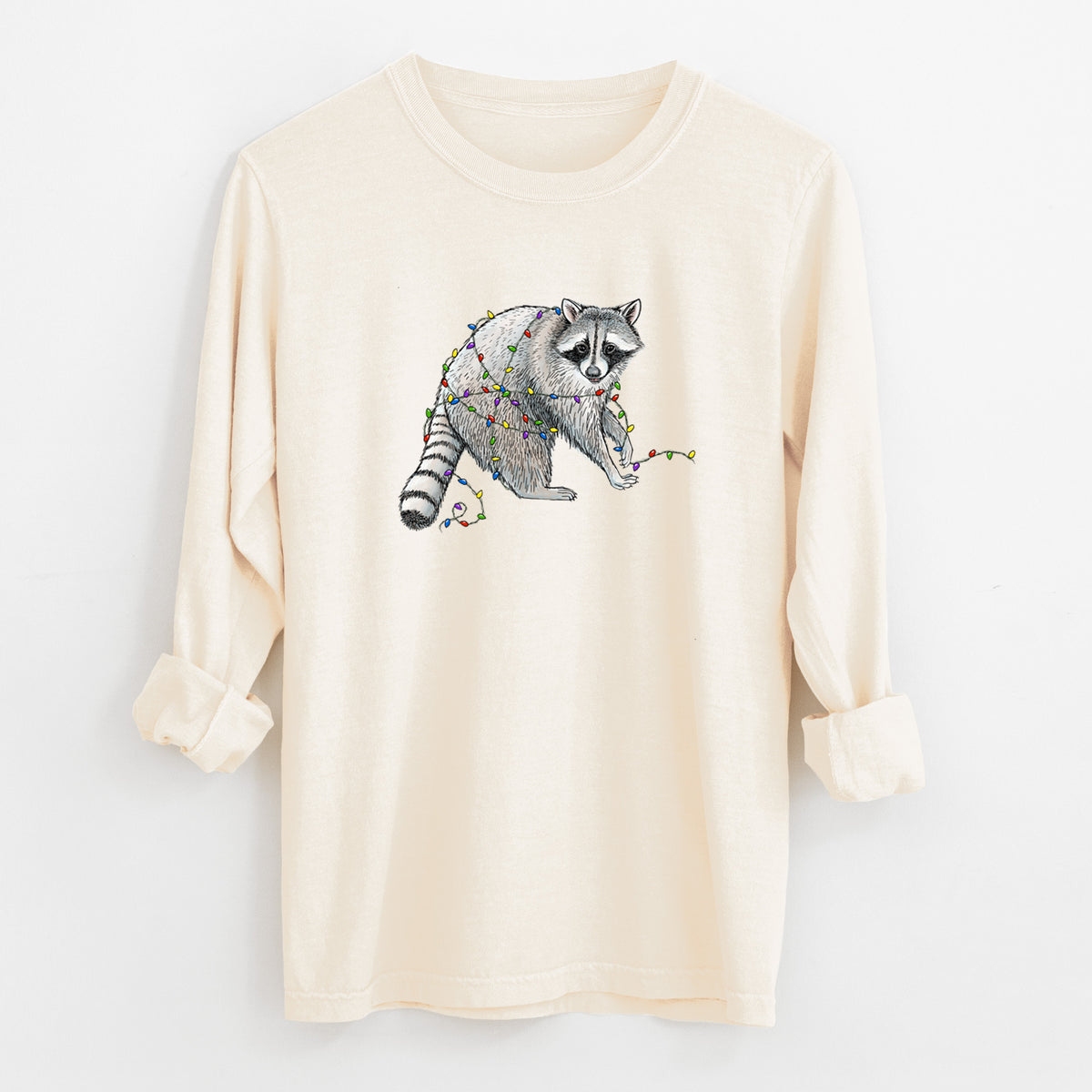 Ivory Comfort Colors long sleeve shirt laid flat with the cuffs rolled, printed with a black ink raccoon tangled in a string of colorful holiday lights.