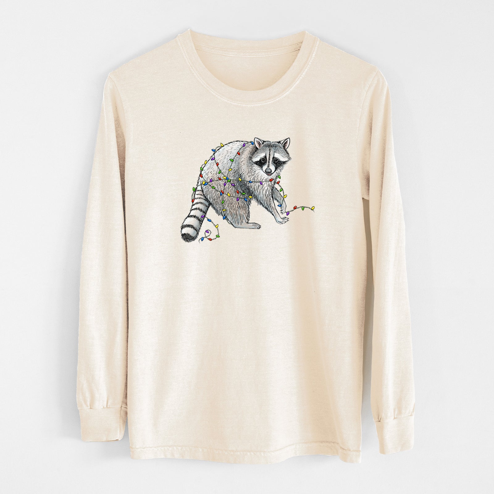 Ivory Comfort Colors long sleeve shirt laid flat, printed with a black ink raccoon tangled in a string of colorful holiday lights.