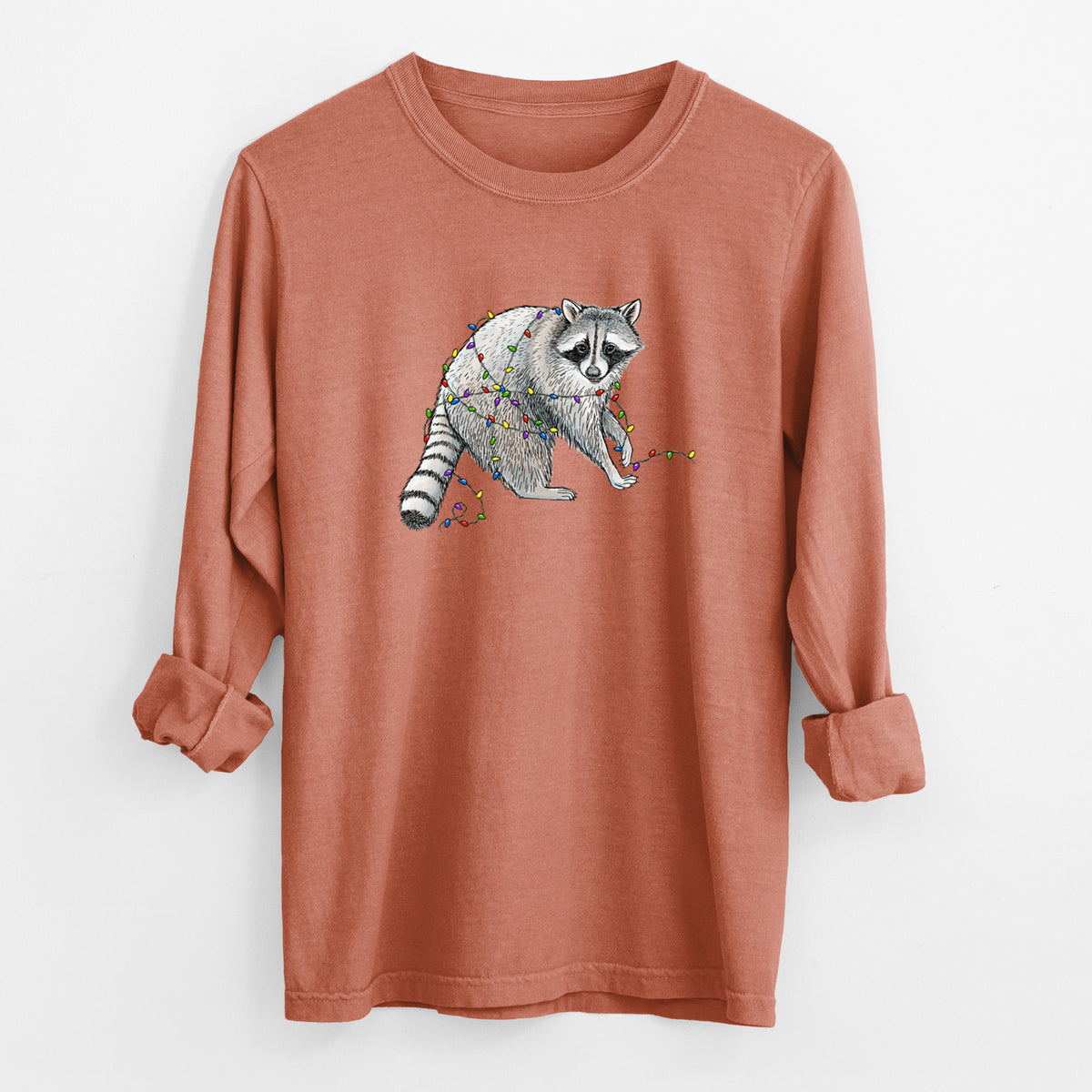 Yam burnt orange Comfort Colors long sleeve shirt laid flat with the cuffs rolled, printed with a black ink raccoon tangled in a string of colorful holiday lights.