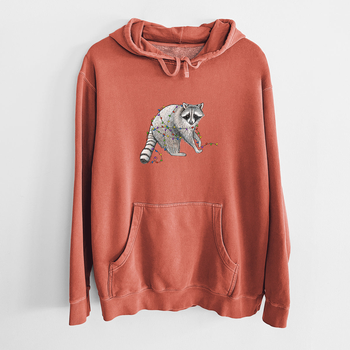 Amber orange pigment dyed hoodie laid flat, printed with a black ink raccoon tangled in a string of colorful holiday lights.
