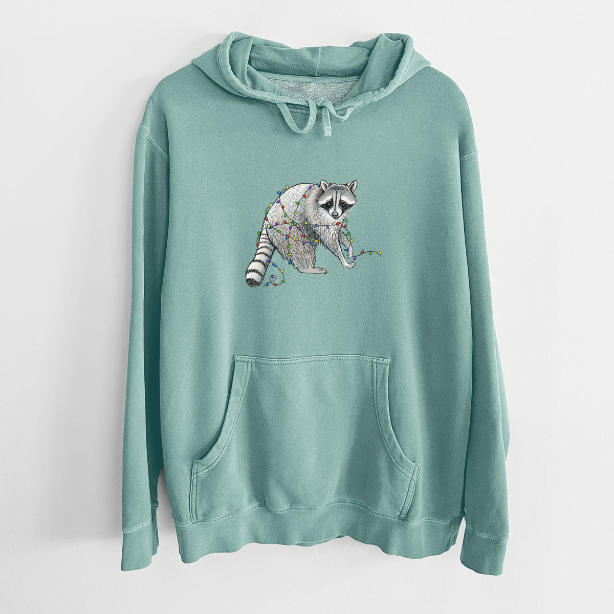 Mint green pigment dyed hoodie laid flat, printed with a black ink raccoon tangled in a string of colorful holiday lights.