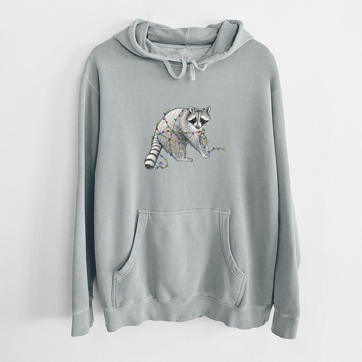 Sage green pigment dyed hoodie laid flat, printed with a black ink raccoon tangled in a string of colorful holiday lights.