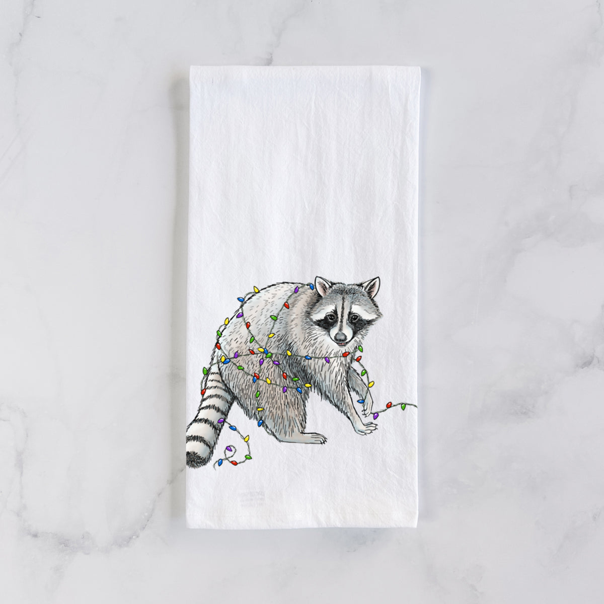 White cotton tea towel laid flat on marble, printed with a black ink raccoon tangled in a string of colorful holiday lights.