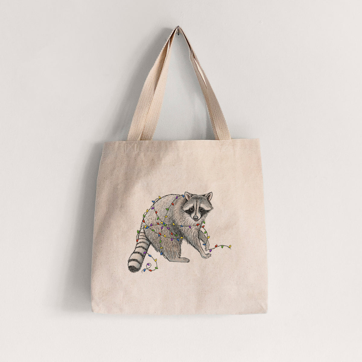 Natural canvas tote bag printed with a black ink raccoon tangled in a string of colorful holiday lights.