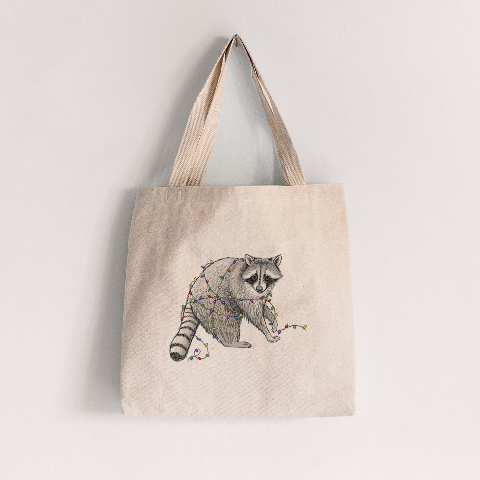 Natural canvas tote bag printed with a black ink raccoon tangled in a string of colorful holiday lights.
