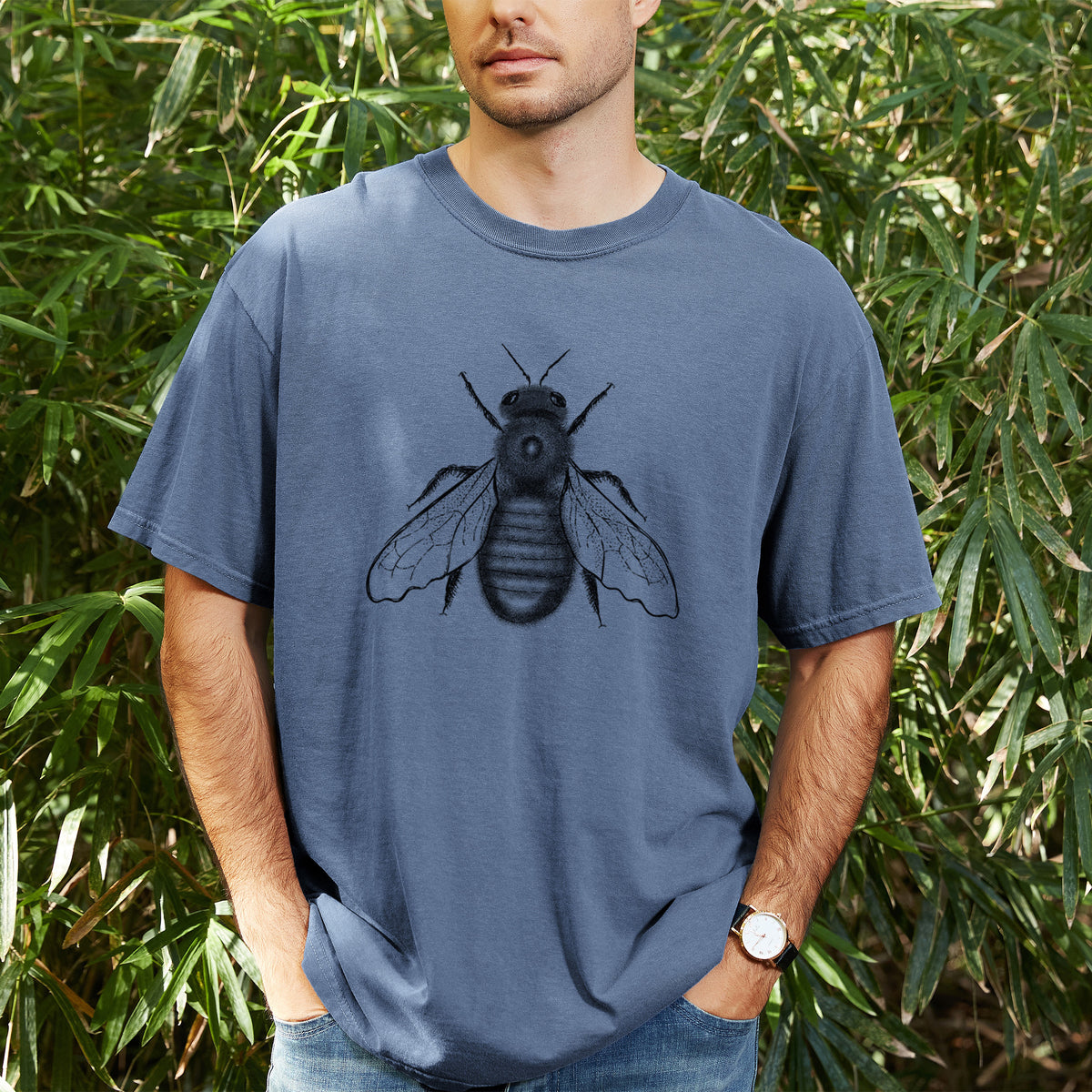 Man wearing a Comfort Colors t-shirt printed with a detailed black ink illustration of an eastern carpenter bee with its wings spread, seen from above, outdoors.