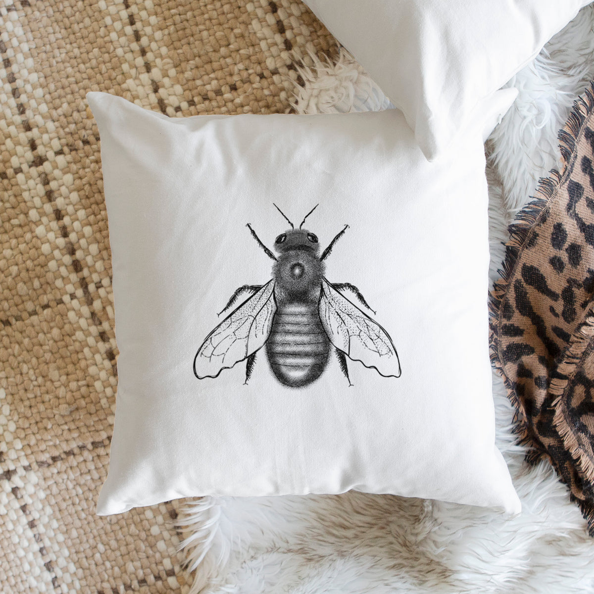 White pillow cover printed with a detailed black ink illustration of an eastern carpenter bee with its wings spread, seen from above, on a woven chair.