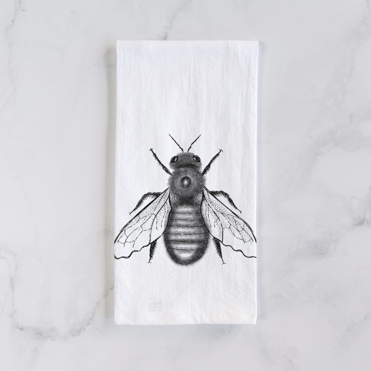 White cotton tea towel laid flat on marble, printed with a detailed black ink illustration of an eastern carpenter bee with its wings spread, seen from above.