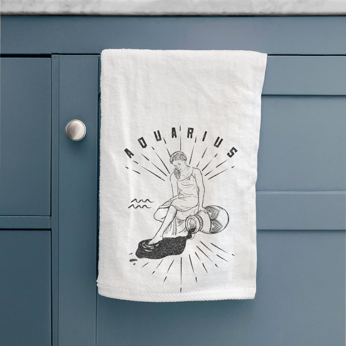 White hand towel printed with a black ink figure pouring water with the word Aquarius, for the Aquarius zodiac sign, hanging on a cabinet door.