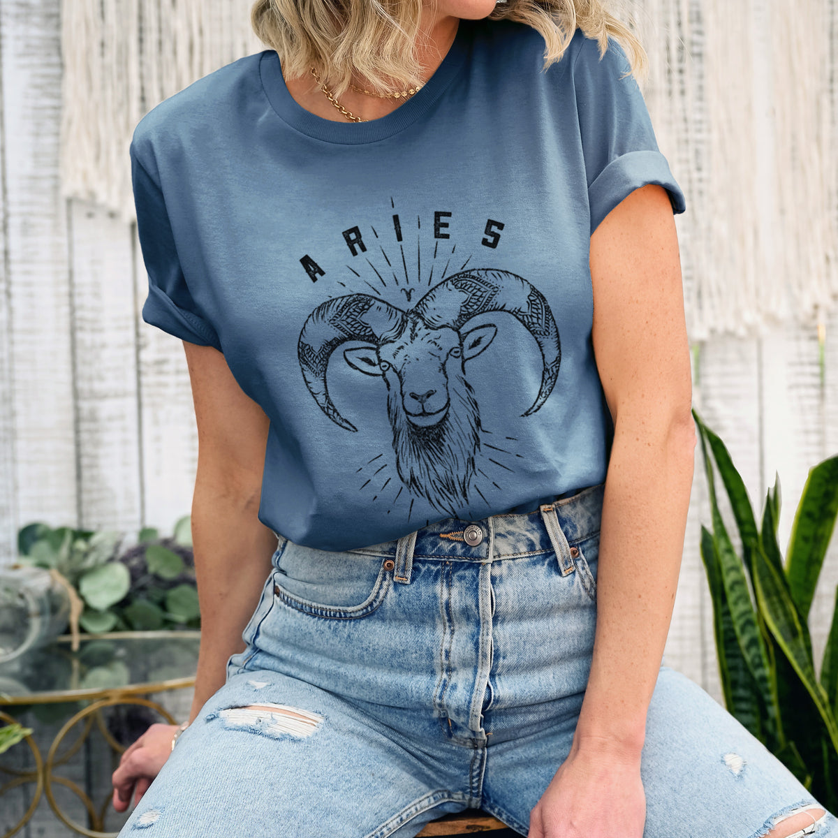 Woman wearing a steel blue lightweight cotton t-shirt printed with a black ink ram's head with curled horns and the word Aries, for the Aries zodiac sign.